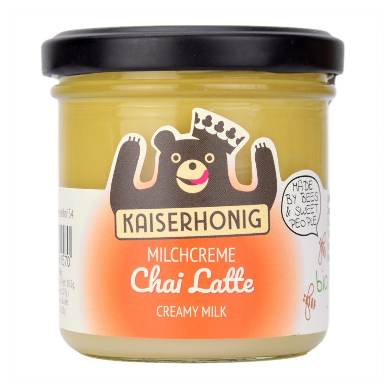 Glas Kaiserhonig Milchcreme Chai Latte mit schwarzem Deckel, orangefarbenem Etikett und fröhlichem Bärenmotiv, Aufschrift „Creamy Milk“ in Weiß.