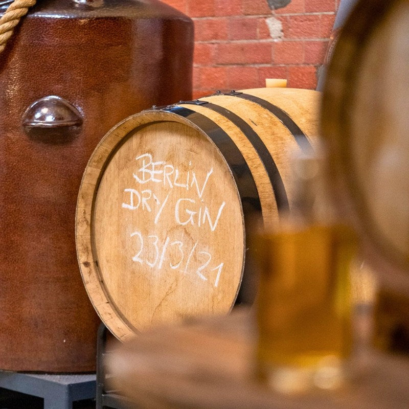 Eichenholzfass mit der Aufschrift "Berlin Dry Gin 23/03/21" in einer Destillerie-Umgebung – zeigt Reifung des Gins.
