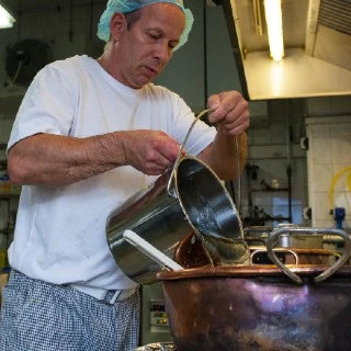 Mitarbeiter der Manufaktur gießt Zuckermasse aus einem kleinen Eimer in einen Kupferkessel.