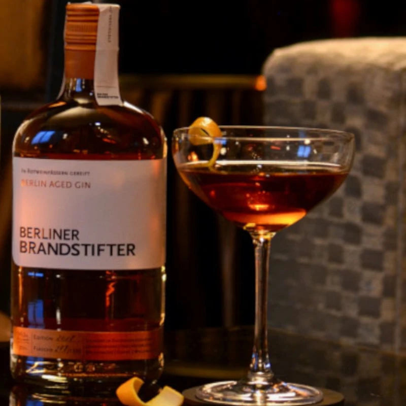 Berliner Brandstifter Aged Gin serviert im Cocktailglas mit Zeste, stimmungsvolle Szene in Bar-Atmosphäre