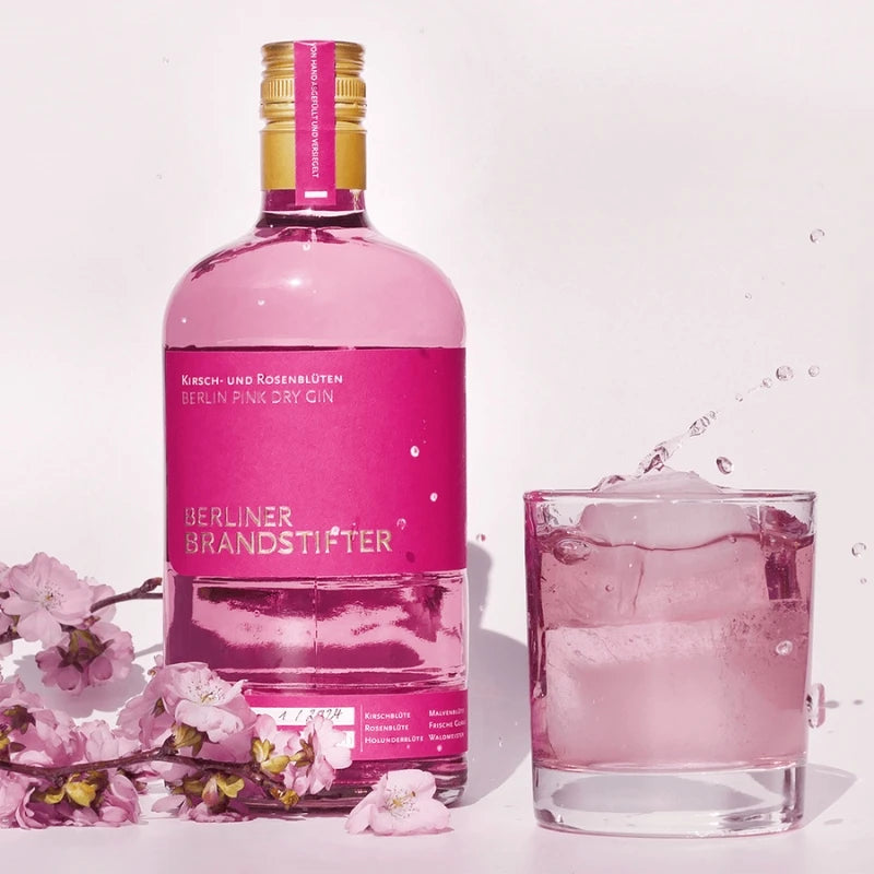 „Berliner Brandstifter Pink Dry Gin mit Cocktailglas, Eiswürfeln und Kirschblüten – stilvolle Szene mit Spritzmoment.“