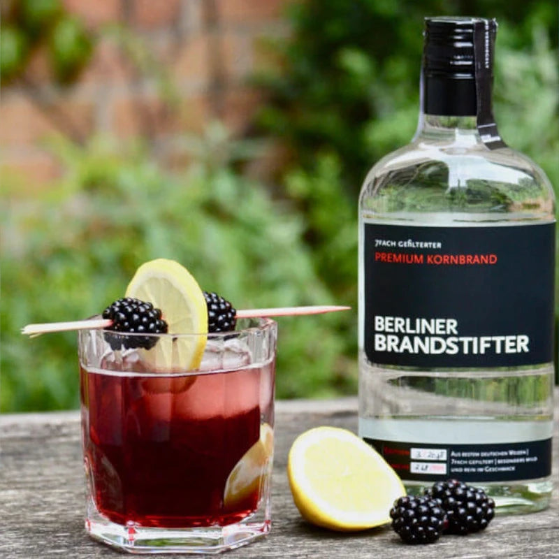 „Serviervorschlag mit Berliner Brandstifter Kornbrand, Cocktail mit Brombeeren und Zitrone auf Holzuntergrund“