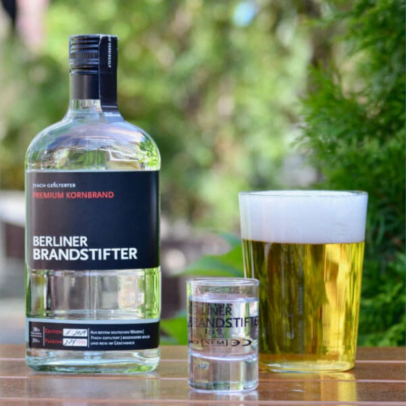 „Berliner Brandstifter Kornbrand neben einem Bierglas und einem Shotglas im Garten serviert“
