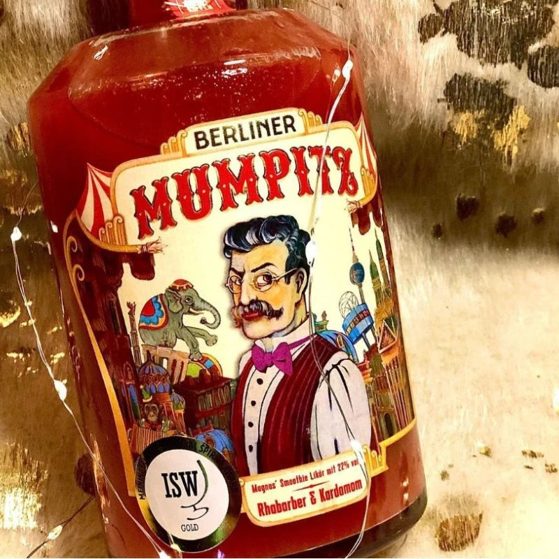 Flasche Berliner Mumpitz Rhabarber & Kardamom mit verspieltem Etikett und ISW-Gold-Siegel, auf dekorativem Untergrund mit Lichterkette und Felloptik inszeniert.