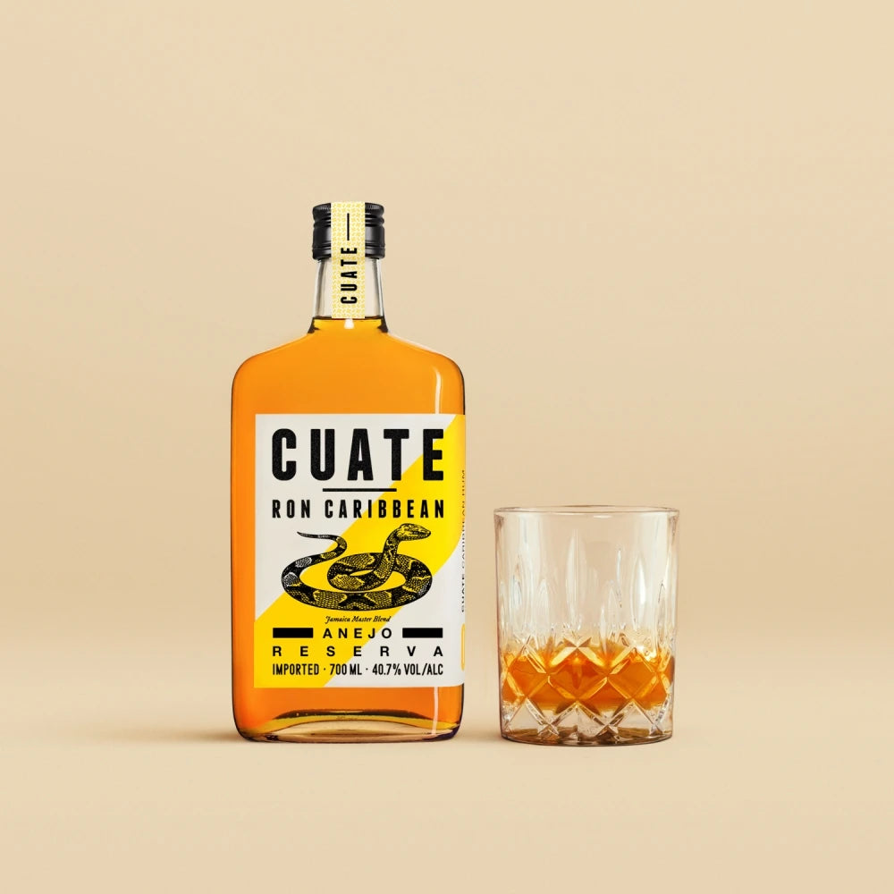 CUATE Rum 04 Añejo Reserva 700 ml neben Kristallglas, Zitrone und tropischem Blatt dekorativ arrangiert.