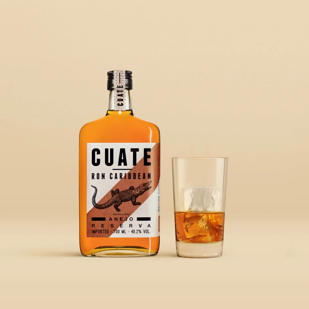 CUATE Rum 06 Añejo Reserva – Produktfoto mit Glas auf hellem Hintergrund, bernsteinfarbener Rum in Flasche und Glas mit Eiswürfeln.