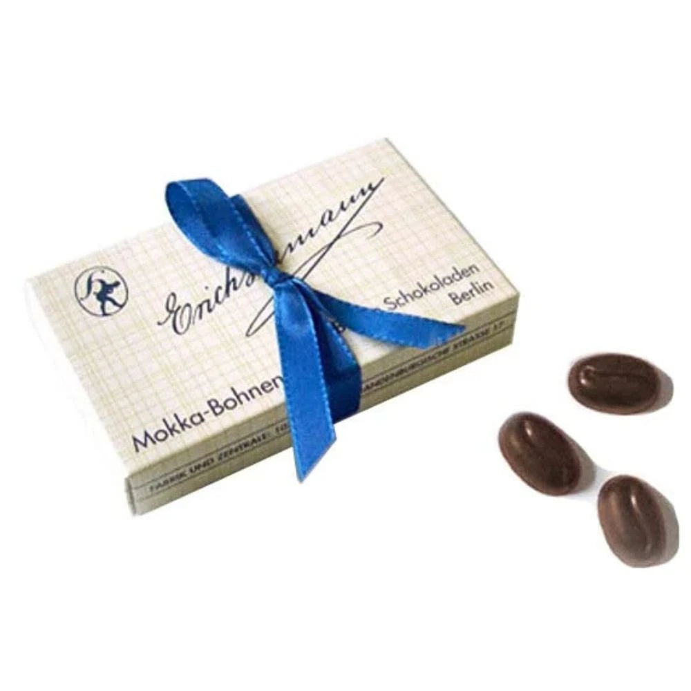 Erich Hamann Mokka-Bohnen – Pralinenschachtel mit blauer Schleife, daneben drei schokolierte Kaffeebohnen. Elegante Berliner Confiserie als Geschenkidee.