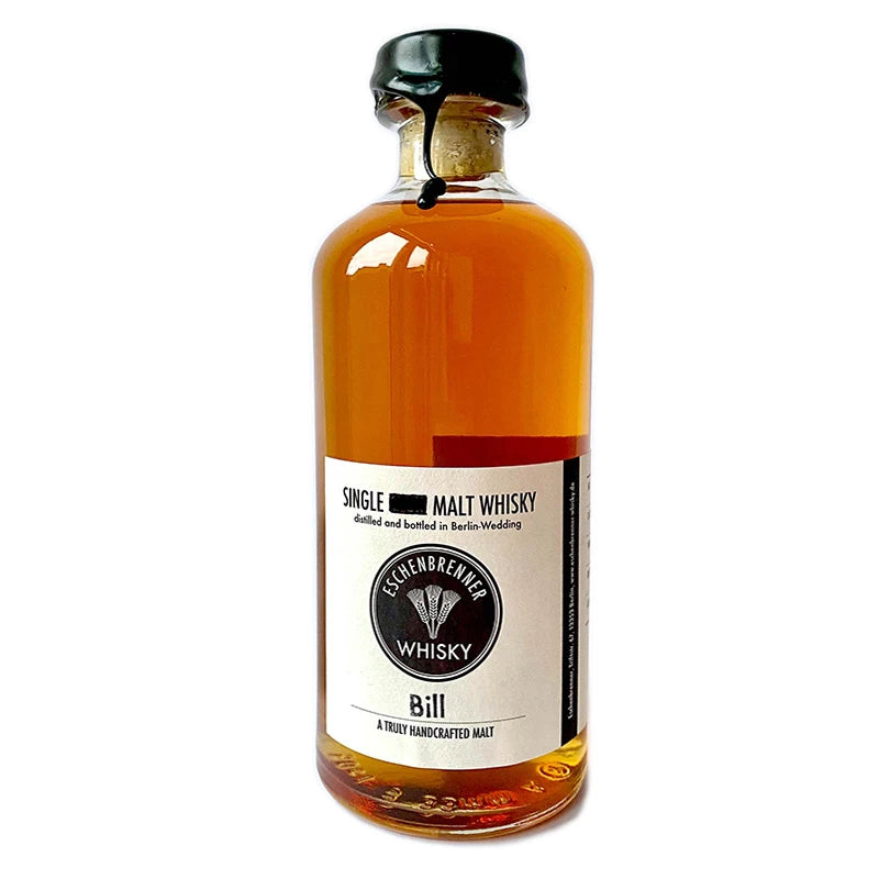 Eschenbrenner Single Malt Whisky „Bill“ in 0,5 l-Flasche mit schwarzem Wachsverschluss und schlichtem Etikett. Aufdruck: „Single Malt Whisky – distilled and bottled in Berlin-Wedding“, darunter Markenlogo und der Schriftzug „Bill – A truly handcrafted malt“. Der Whisky zeigt eine warme, bernsteinfarbene Tönung.