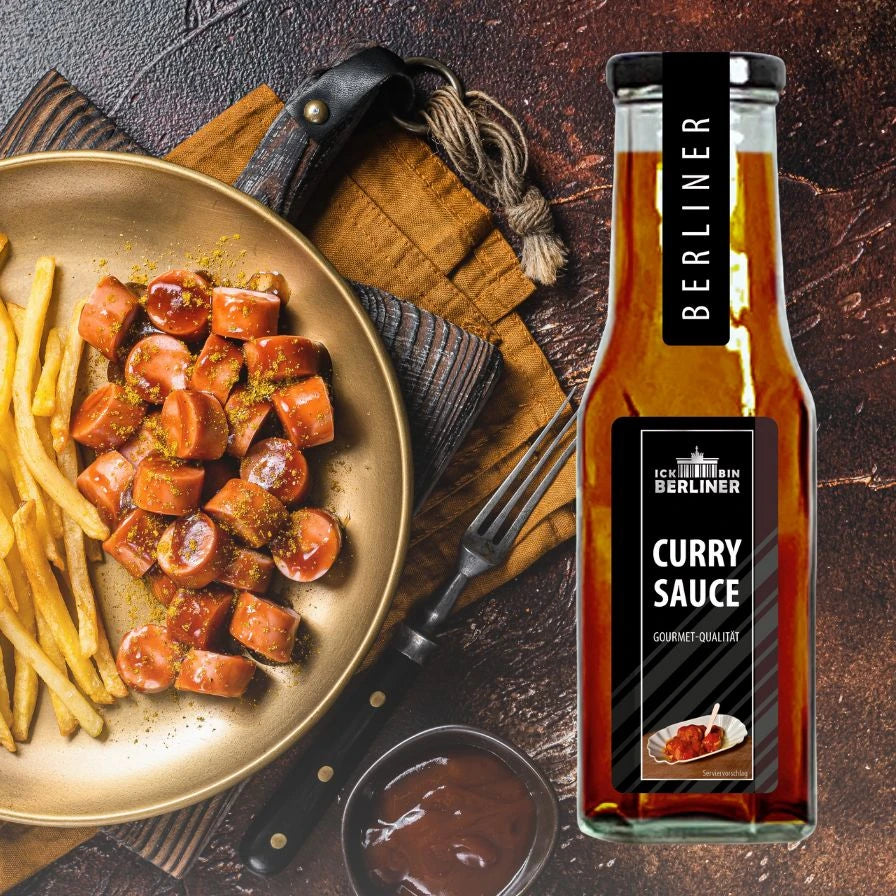 Currywurst mit Pommes angerichtet in bronzefarbener Pfanne, flankiert von ICK BIN BERLINER Curry Sauce. Berliner Spezialität, stilvoll in Szene gesetzt.