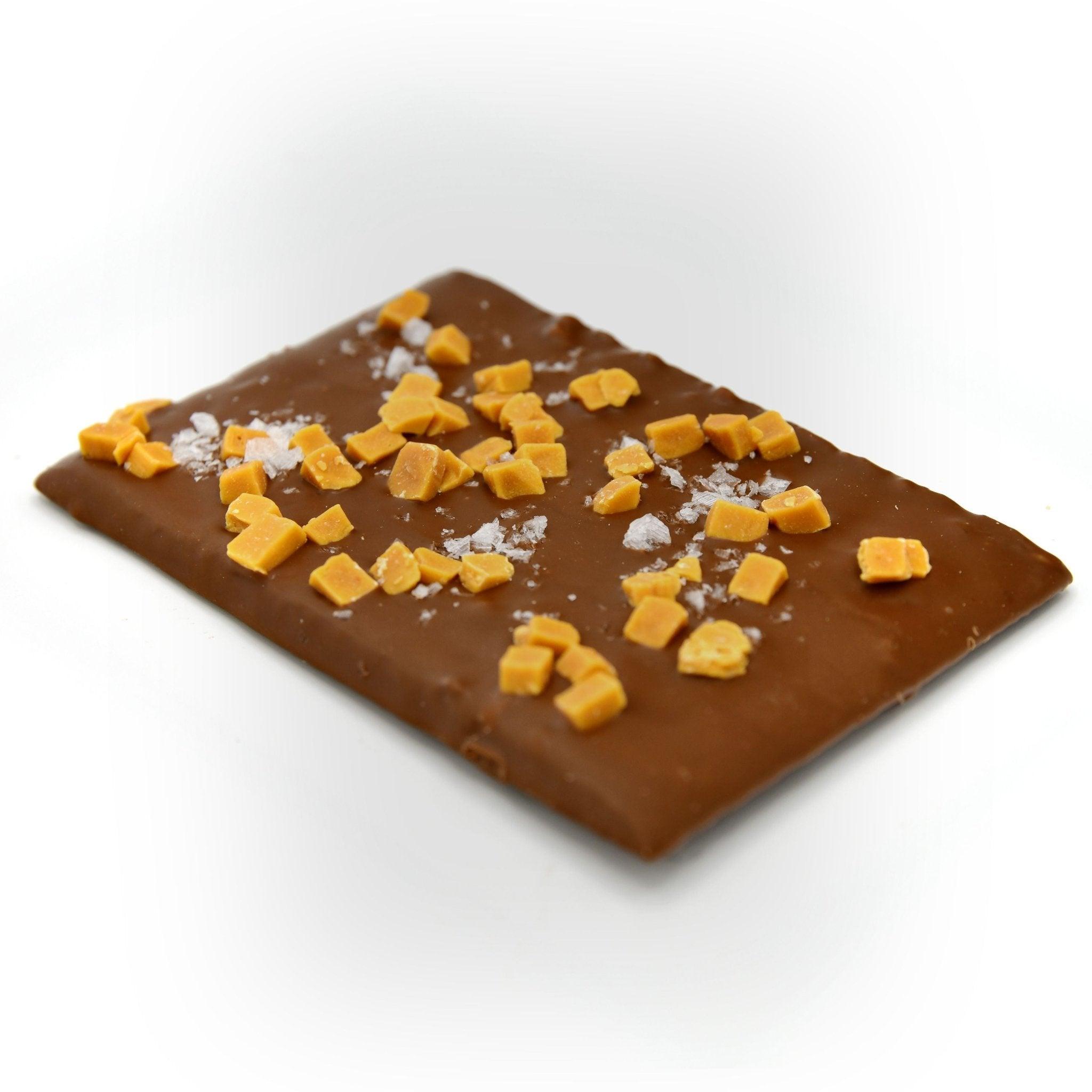 Handgefertigte Vollmilchschokolade mit goldenen Karamellstückchen und Meersalz – diagonale Perspektive, Berliner Manufakturqualität.