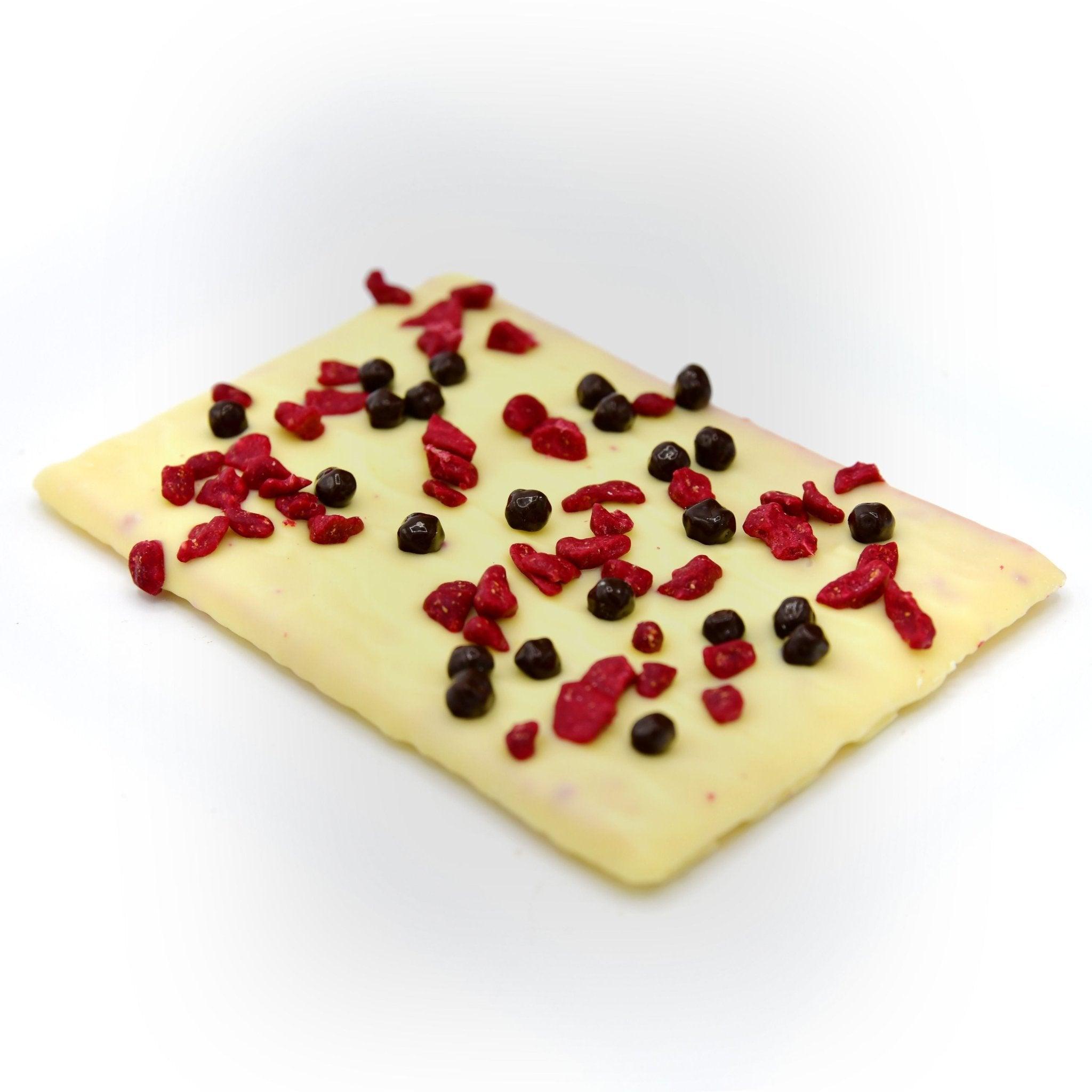 Weiße Manufaktur-Schokolade mit gefriergetrockneten Himbeerstückchen und knusprigen Schokoperlen – diagonale Ansicht, handgemacht in Berlin.