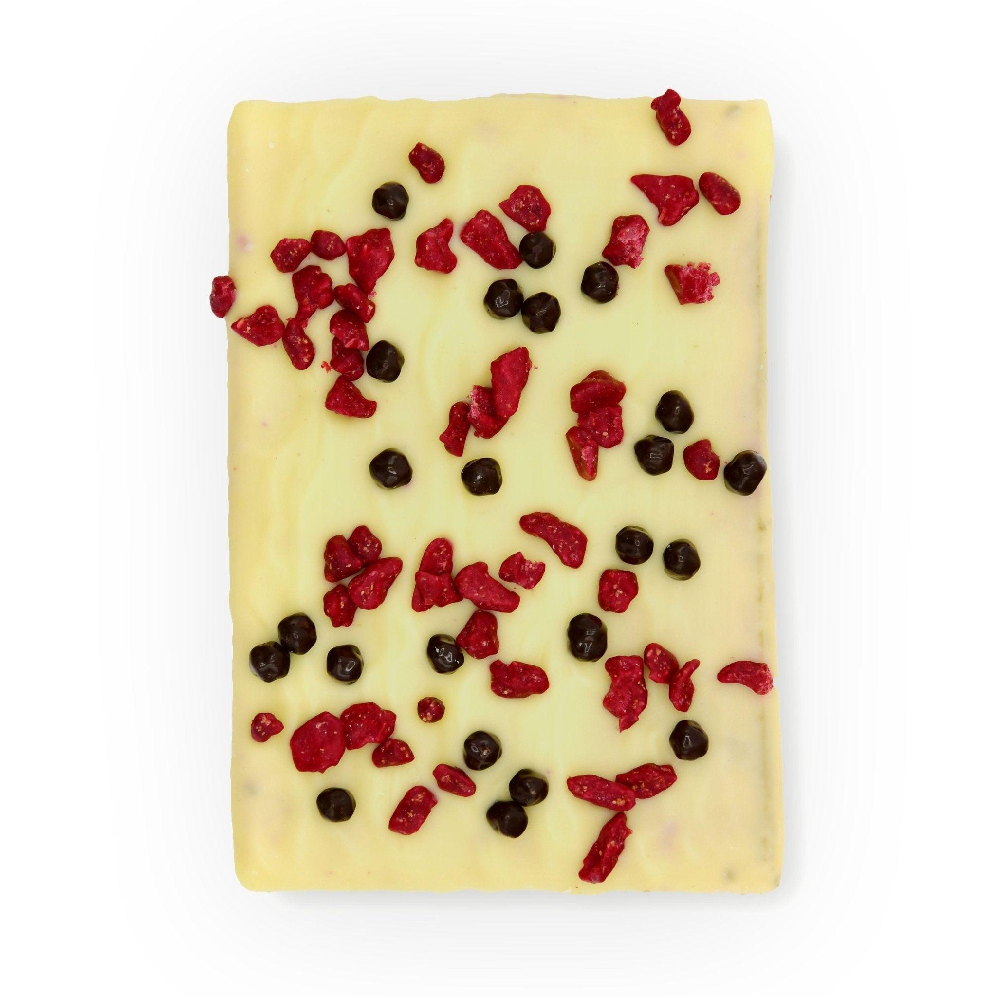 Obenansicht einer weißen Schokoladentafel mit fruchtigen Himbeerstückchen und dunklen Schokoperlen – Berliner Manufakturqualität pur.