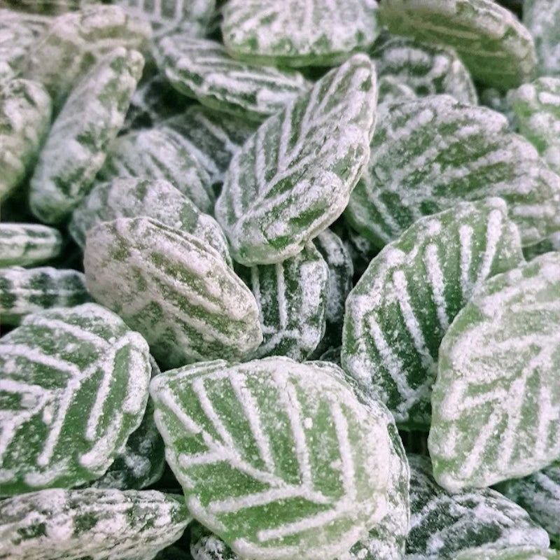 Nahaufnahme grüner Bonbons in Blattform mit feinem Zuckermantel, deutlich sichtbare Struktur und klassische Prägung.