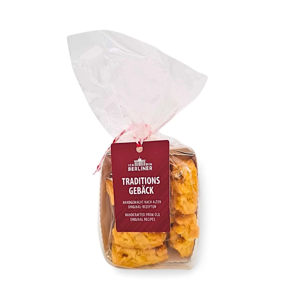 Tüte mit Butterstreusel-Gebäck von ICK BIN BERLINER, liebevoll verpackt in einer durchsichtigen Folie mit rot-weißem Band und rotem Etikett mit der Aufschrift „Traditionsgebäck – handgemacht nach alten Original-Rezepten“.