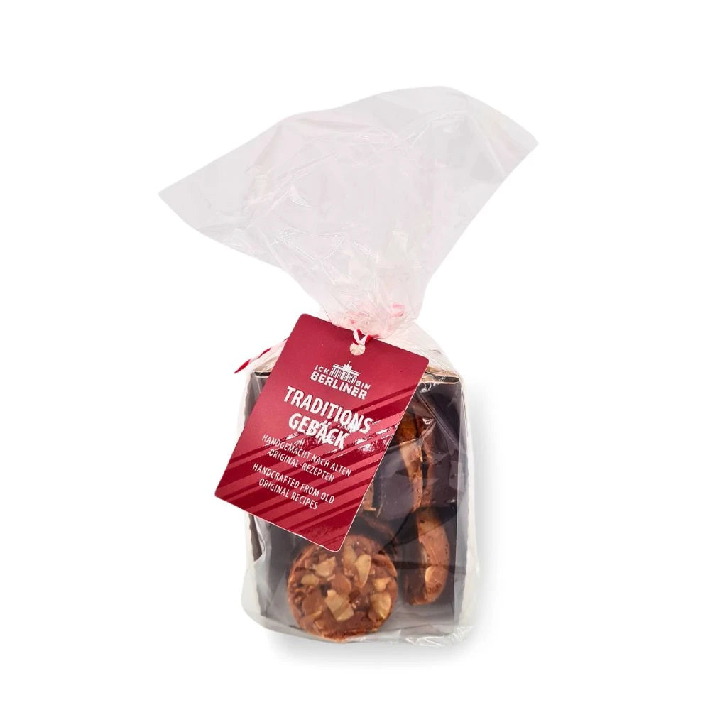 Klarsichtverpackung mit rot-weißem Band und Anhänger der Marke „ICK BIN BERLINER“, gefüllt mit handgemachten Florentinern aus Mandelblättchen und dunkler Schokolade, traditionell gebacken nach Berliner Originalrezepten.