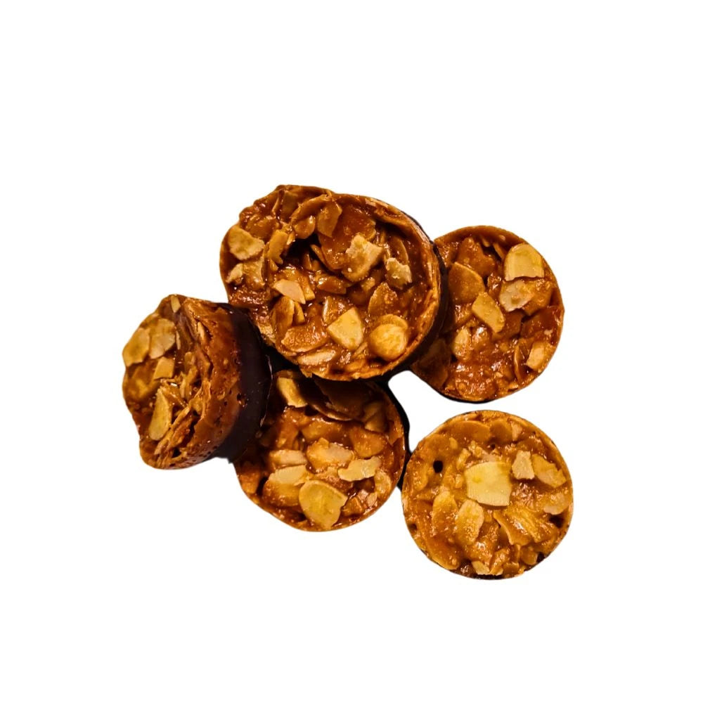 Fünf goldbraune Florentiner mit karamellisierten Mandelblättchen und einem Boden aus dunkler Schokolade, sorgfältig von oben fotografiert.