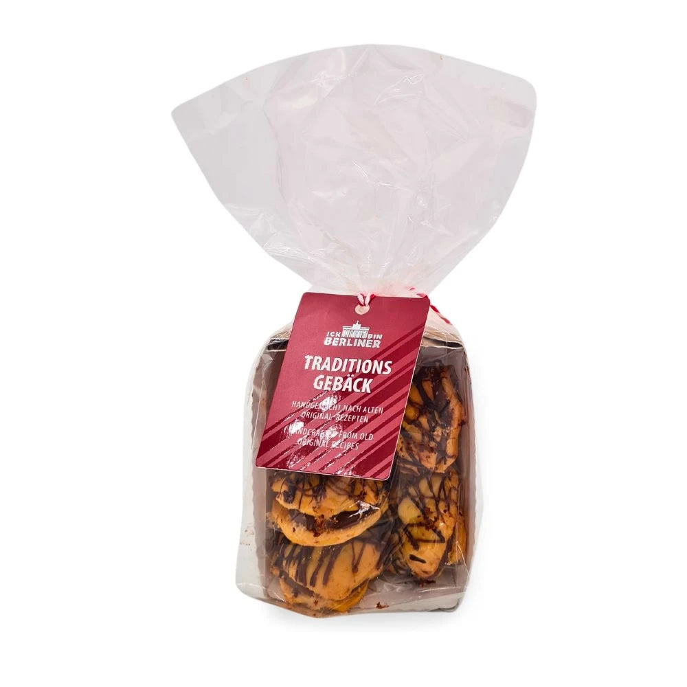 Transparenter Beutel mit rot-weißem Band und Etikett von „ICK BIN BERLINER“ mit der Aufschrift „Traditionsgebäck“; sichtbar sind handgefertigte Nougatmuscheln mit feiner Schokoladenglasur.