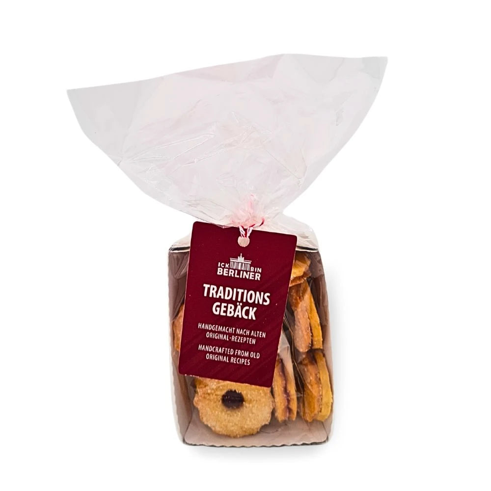 Transparente Tüte mit rot-weißem Band, gefüllt mit handgefertigten Spitzbuben von ICK BIN BERLINER; vorne hängt ein dunkelrotes Etikett mit der Aufschrift "Traditionsgebäck – handgemacht nach alten Original-Rezepten".