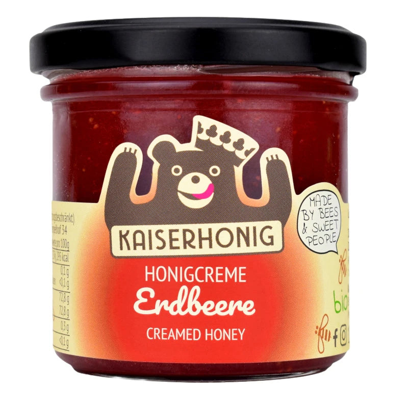 Rotes Honigglas der Marke Kaiserhonig mit schwarzem Deckel und einem Etikett in Erdbeerrot, Aufschrift „Honigcreme Erdbeere – Creamed Honey“, verziert mit einem fröhlichen Bären mit Krone.