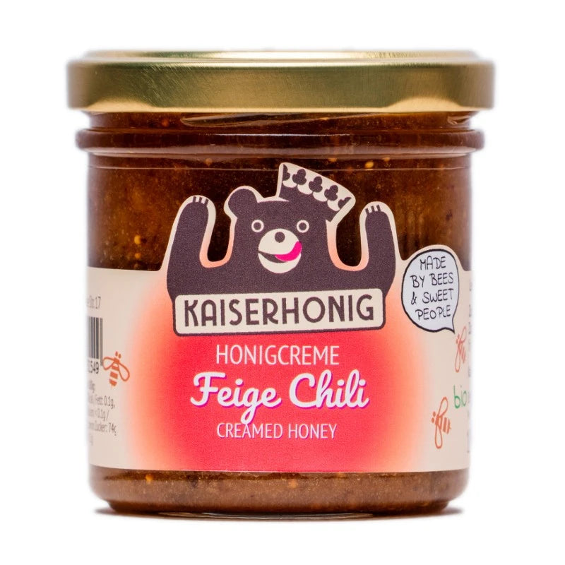 Braunes Honigglas der Marke Kaiserhonig mit goldenem Deckel und leuchtendem Etikett in Pink- und Rottönen, Aufschrift „Honigcreme Feige Chili – Creamed Honey“, verziert mit fröhlichem Bärenlogo.