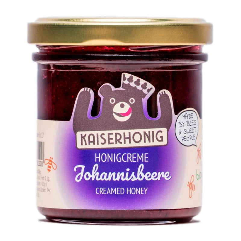 Honigcreme mit Johannisbeere im 180g-Glas von Kaiserhonig, goldener Deckel, lila Etikett mit dem Markenbären und dem Slogan „Made by bees & sweet people“.