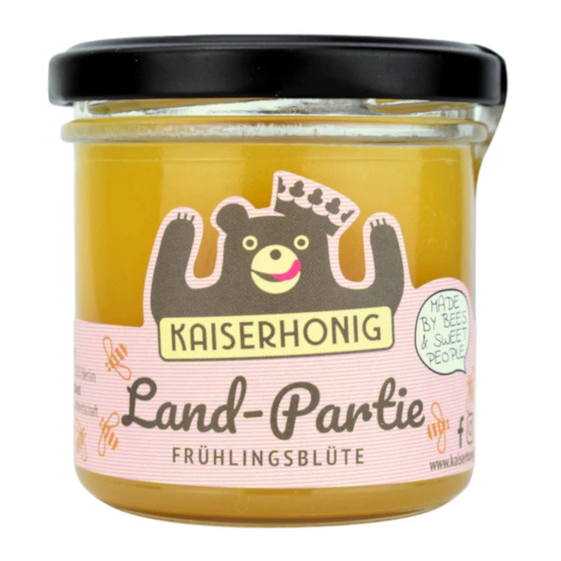 Honigglas mit schwarzem Deckel und rosafarbenem Etikett der Marke Kaiserhonig, dekoriert mit einem lächelnden Bären mit Krone; Aufschrift „Land-Partie Frühlingsblüte – Made by bees & sweet people“.