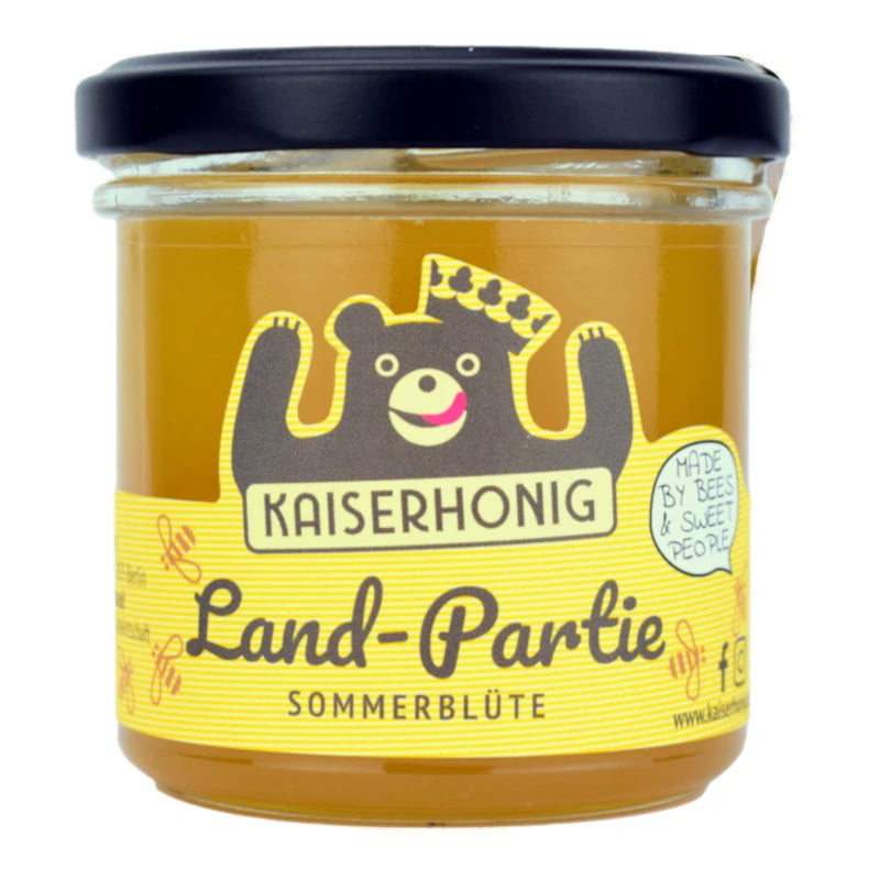 Honigglas der Marke Kaiserhonig mit schwarzem Deckel und gelbem Etikett, verziert mit einem fröhlichen Bären mit Krone; Aufschrift „Land-Partie Sommerblüte – Made by bees & sweet people“.