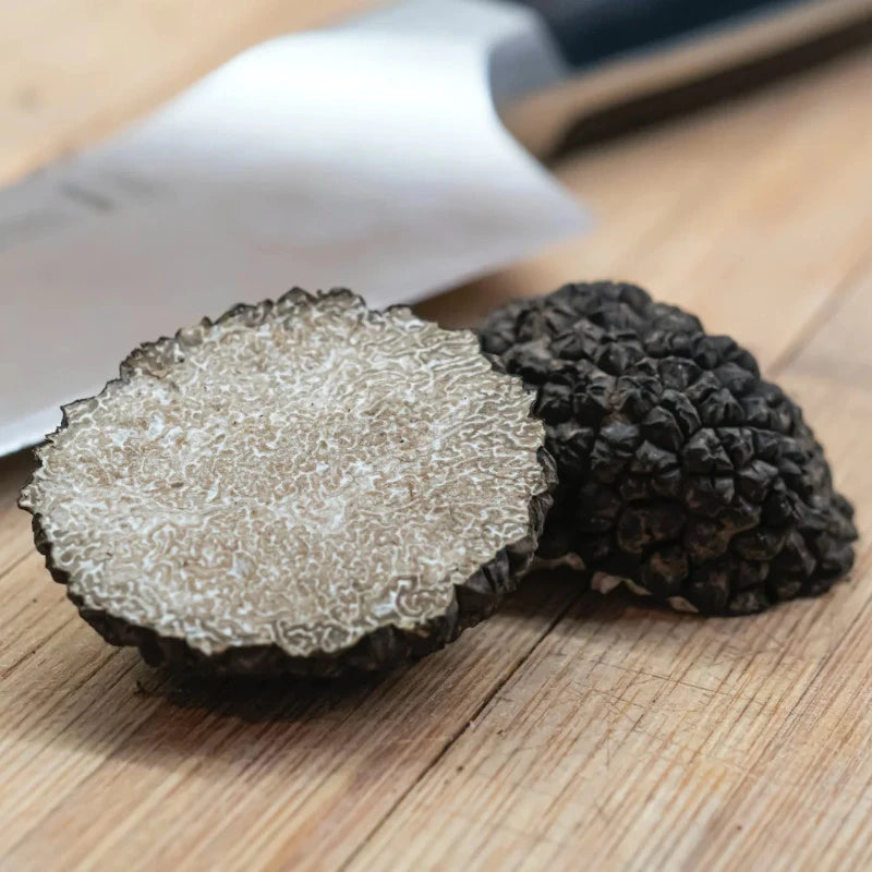 Schwarzer Trüffel, halbiert, auf Holzbrett neben Küchenmesser – edle Zutat für das aromatische Popcorn aus der Berliner Popkornditorei.