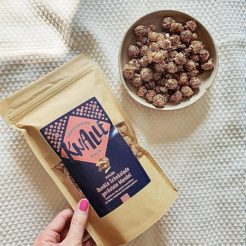 Knalle Popkorn Dunkle Schokolade & Geröstete Mandel im braunen Standbeutel und als Portion in Schale serviert – ideal für gemütliche Genussmomente.