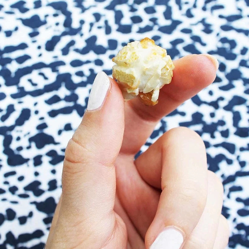 Nahaufnahme: Popcornstück mit Kokosraspeln wird zwischen zwei Fingern gehalten – perfekte Berliner Knabberei mit feiner Süße.