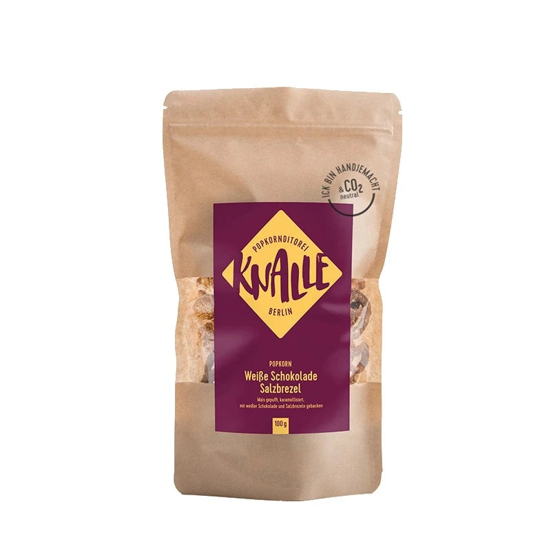 Knalle Popkorn Weiße Schokolade Salzbrezel, 100 g im braunen Standbeutel mit burgunderfarbenem Etikett. Handgemacht in Berlin, CO₂-neutral produziert.