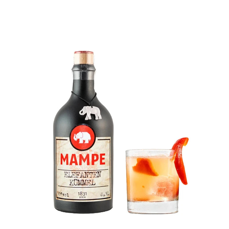 Mampe Elefanten Kümmel Flasche neben einem Tumbler-Glas mit Eis, orangefarbener Flüssigkeit und Paprikastreifen-Garnitur. Der Cocktail hebt die würzig-aromatische Note des Kümmellikörs hervor.