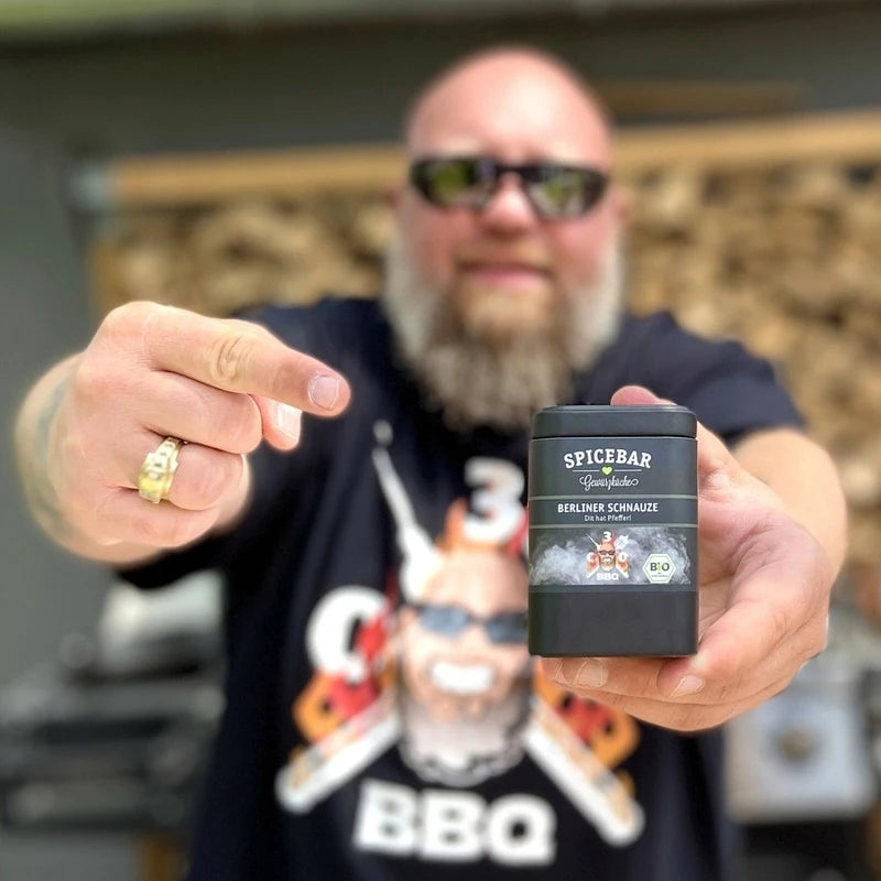 Bärtiger Mann mit Sonnenbrille und BBQ-Shirt präsentiert die Spicebar-Gewürzdose „Berliner Schnauze“ in die Kamera.
