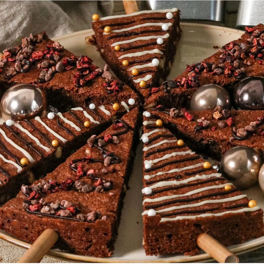 Dekorativ angerichtete Stücke von schokoladigem Kuchen mit essbarer Deko, Schokoladensplittern und Glanzperlen auf einem runden Teller.