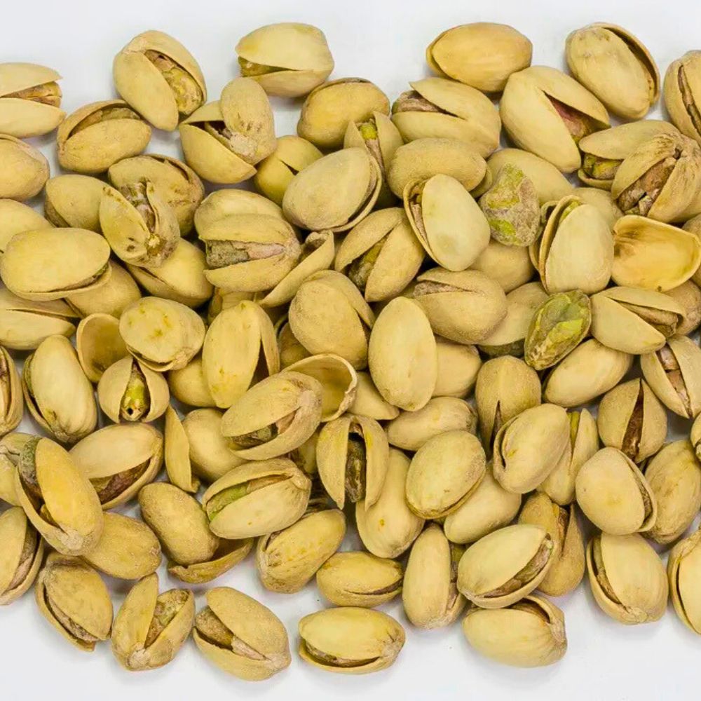 Geöffnete, goldbraun geröstete Pistazien mit grünem Kern und groben Meersalzkristallen in Nahaufnahme.