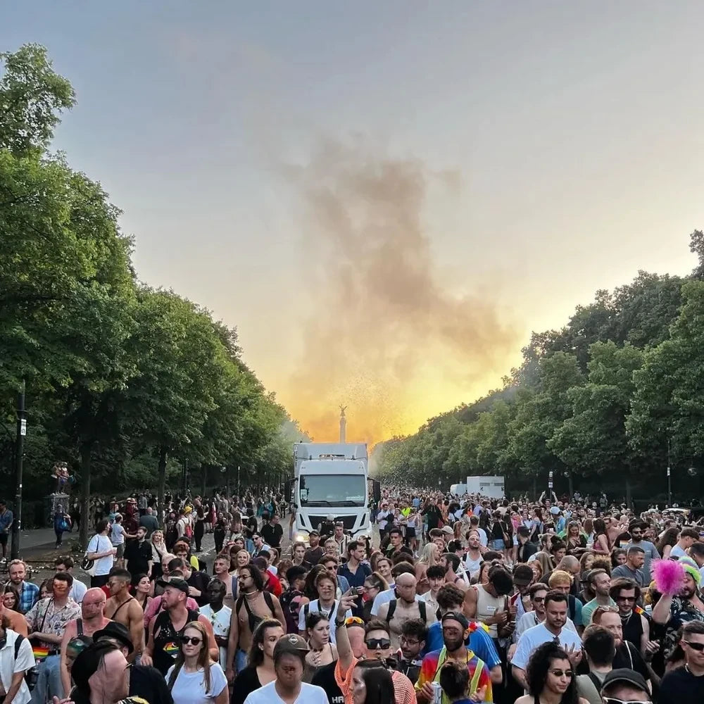 Große Menschenmenge beim Berliner CSD, bunte Pride-Atmosphäre mit Musik und Paradefahrzeugen, Sonnenuntergang über der Straße des 17. Juni Richtung Siegessäule